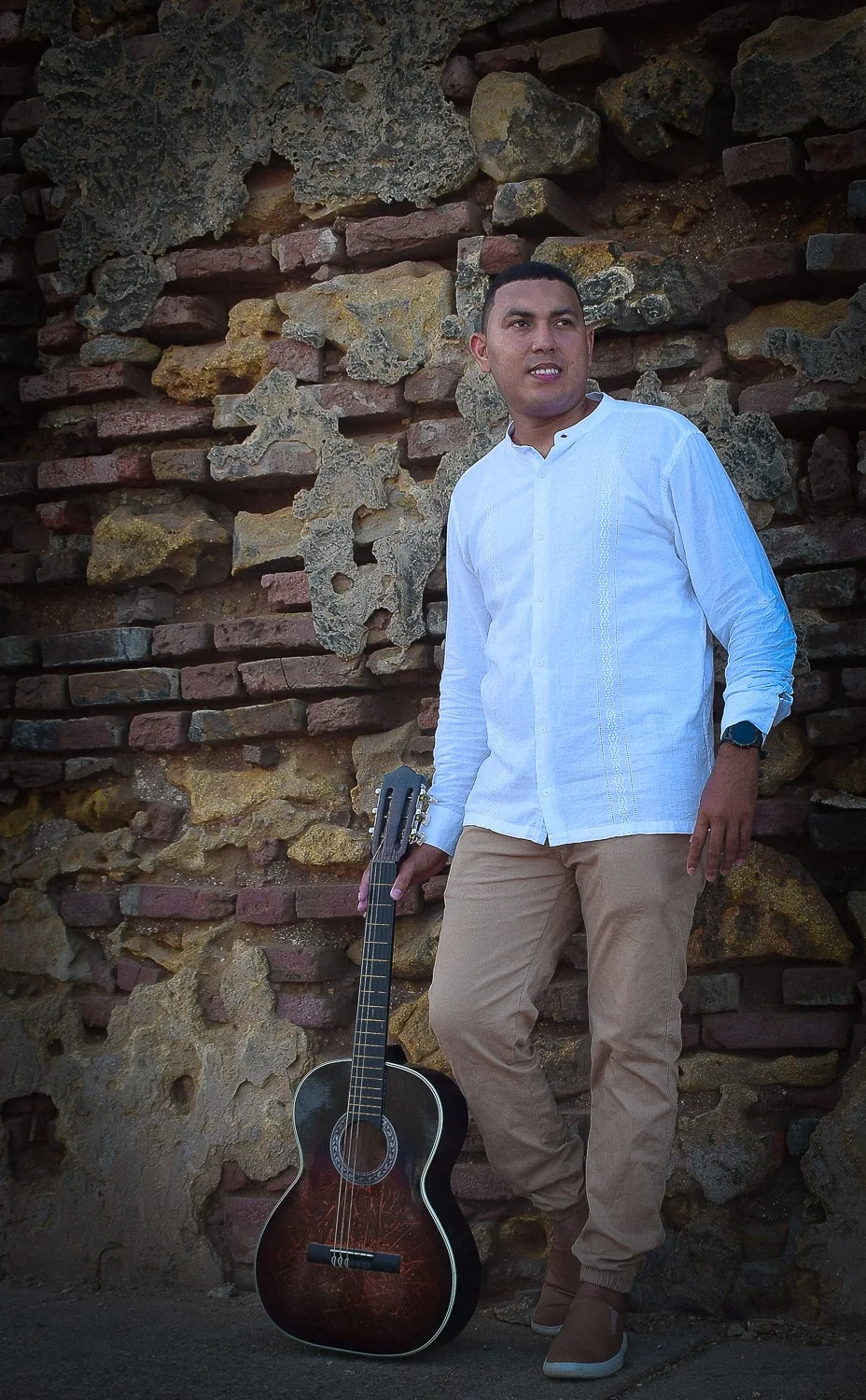 Carlos Andrés con su guitarra frente a un muro de piedra